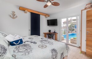 Ein Schlafzimmer mit Bett, Schreibtisch, Fernseher und Blick auf einen Swimmingpool.