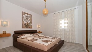 Un dormitorio con una cama grande, un televisor montado en la pared, una lámpara decorativa y cortinas traslúcidas.