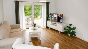 A living room with a sofa, a coffee table, a TV on a white stand, and a potted plant. - Cozy apartment in Passow OT Charlottenho (Passow OT Charlottenho)