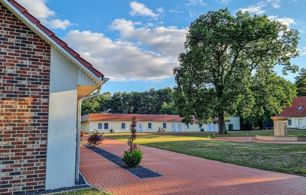 A courtyard with a brick building, a large tree, and a grassy area. - Cozy apartment in Passow OT Charlottenho (Passow OT Charlottenho)