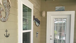 Eine überdachte Veranda mit Deckenventilator, einer Tür mit einem 'Welcome'-Schild und einem Sessel mit Kissen.