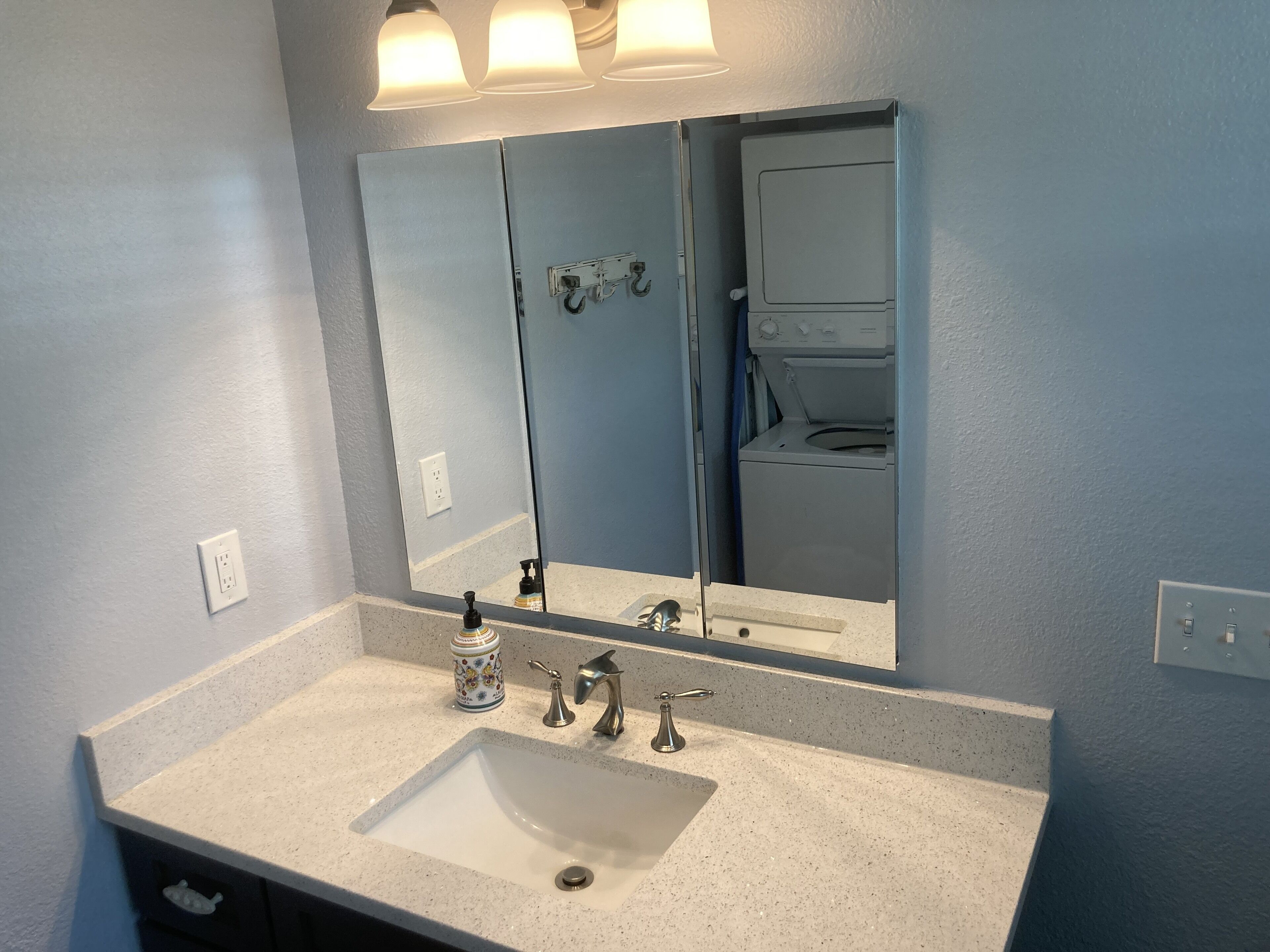 A bathroom with a large mirror, a sink, and a washing machine in the background.