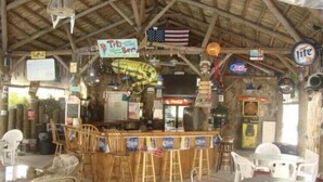 Eine rustikale Bar mit Holzmöbeln, einer amerikanischen Flagge und einem Neon-Schild für 'Tiki Bar'.