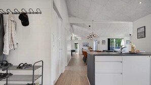 A modern kitchen with a central island, a dining area with chairs, and a hallway with a shoe rack. - Lovely home in Glesborg with sauna (Glesborg)