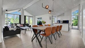 A spacious living area with a dining table, modern furniture, and large windows offering a view of greenery. - Lovely home in Glesborg with sauna (Glesborg)