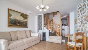 Ein Wohnzimmer mit einem beigen Sofa, einem Holzesstisch mit Stühlen, einer Treppe und einer Küche im Hintergrund.