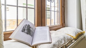 Ein offenes Buch auf einem Bett in der Nähe eines Fensters mit Blick auf Gebäude.