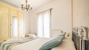 Ein Schlafzimmer mit einem Bett, einer Kommode, einem Heizkörper, einer Deckenleuchte und einem Fenster mit Vorhängen.