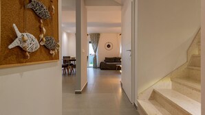 Ein Flur, der in einen Wohnbereich mit Treppe, Essbereich und einer Wand mit dekorativen Muscheln führt.