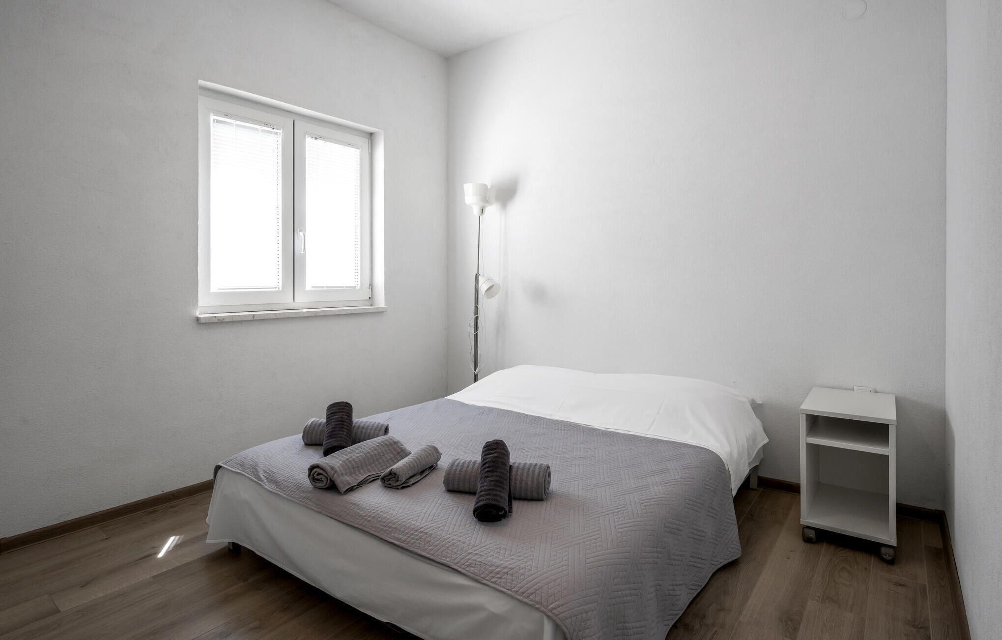 Una camera da letto minimalista con un letto, un comodino, una lampada da terra e una finestra.