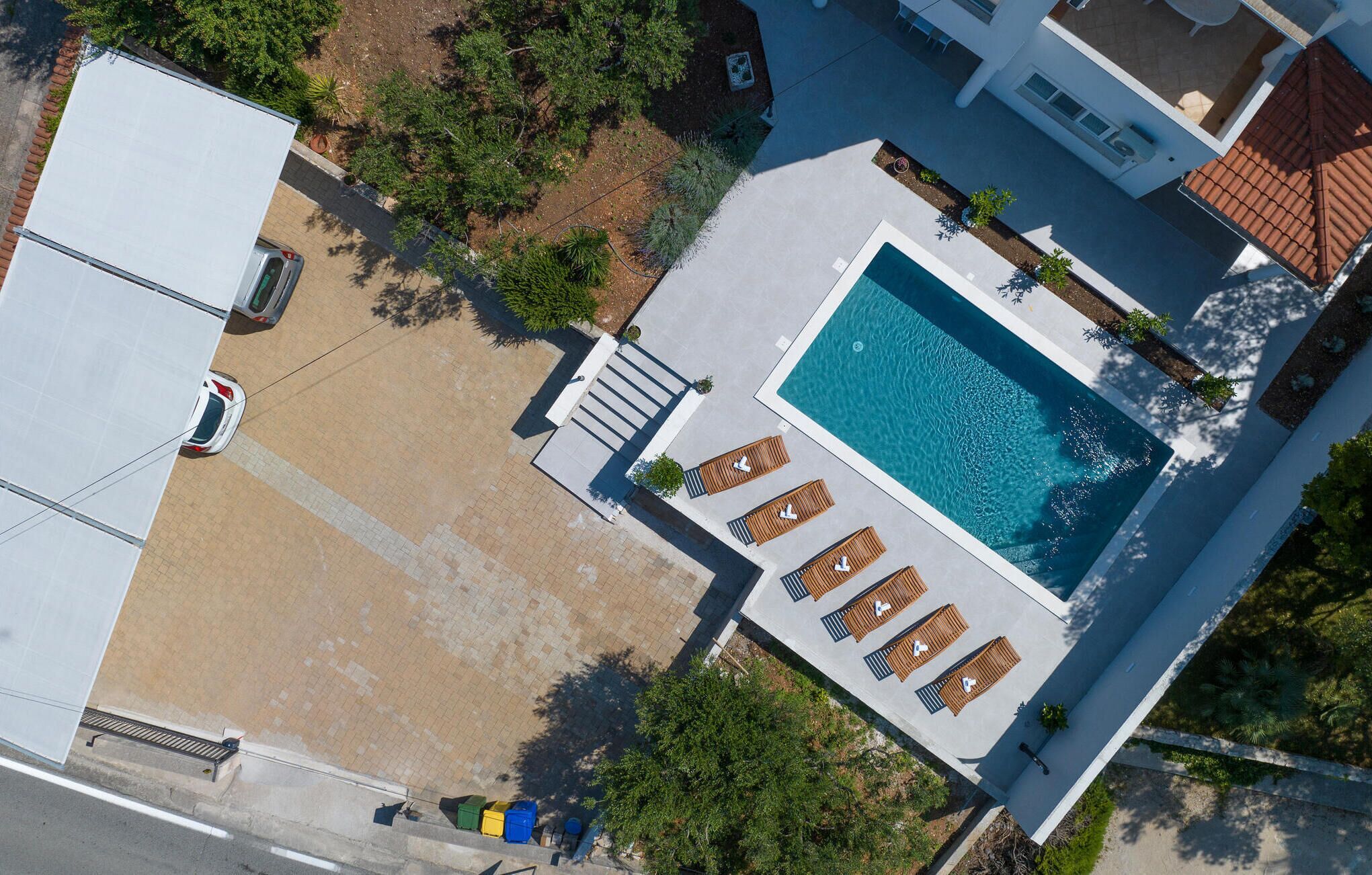 An aerial view of a residential property with a swimming pool, lounge chairs, and a garden area.