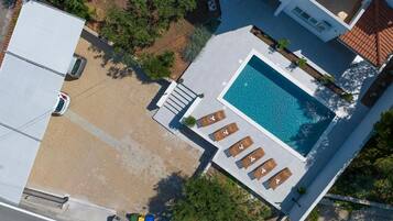 An aerial view of a residential property with a swimming pool, lounge chairs, and a garden area.