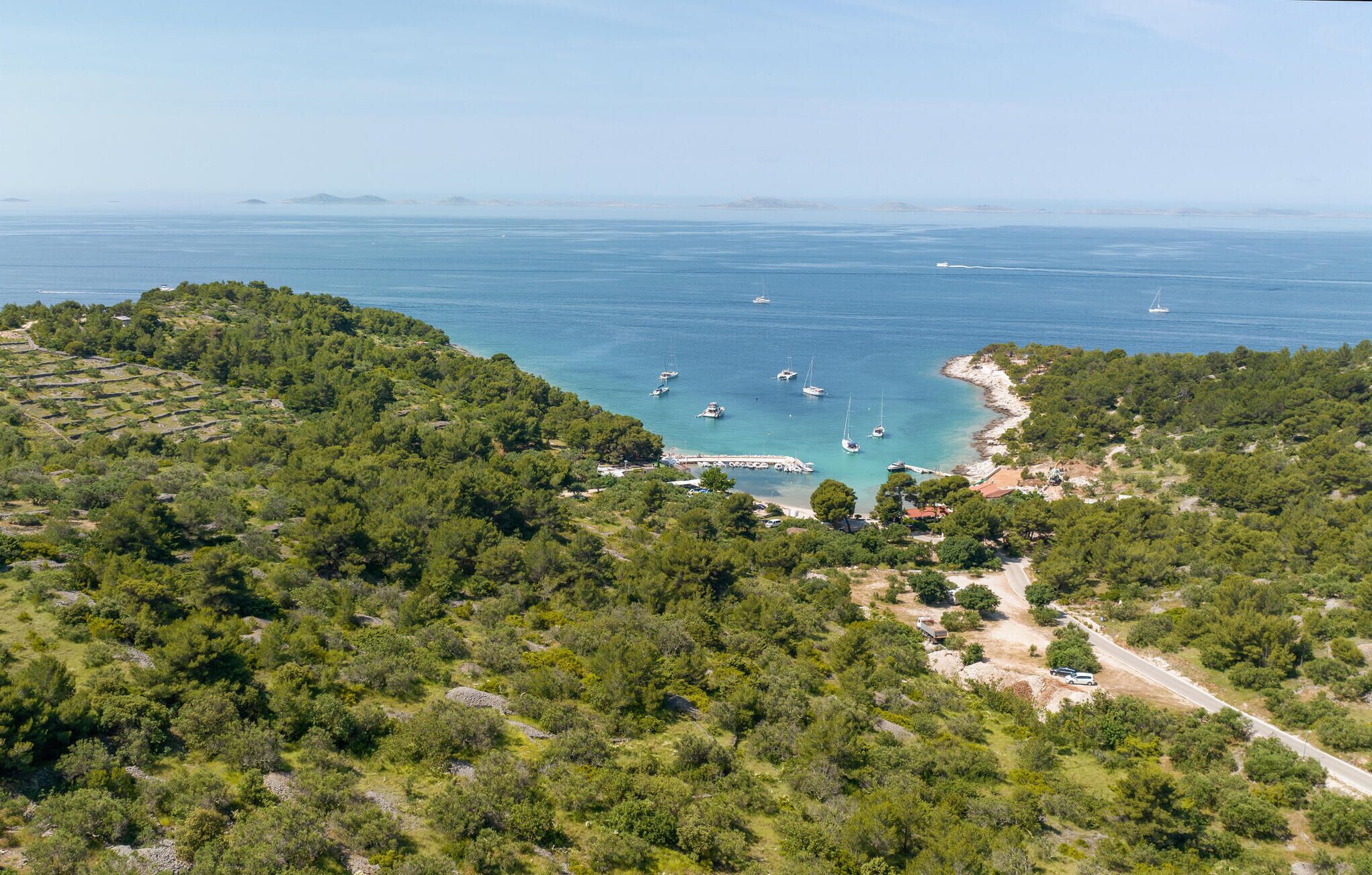 A coastal landscape with a marina, dense greenery, and a clear view of the sea.