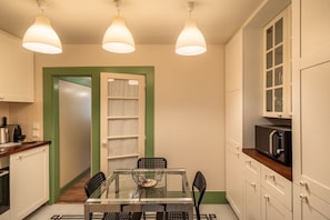 A compact kitchen with a dining table, three pendant lights, and a microwave.