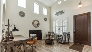 Uma sala de estar ampla com lareira, poltronas estampadas, mesa de centro de madeira e um espelho grande na parede.