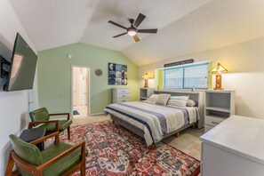 Une chambre à coucher comprenant un lit, un bureau, une chaise, un ventilateur de plafond et une fenêtre avec des stores.