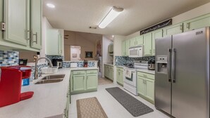 A kitchen with green cabinets, a stainless steel refrigerator, a microwave, and a sink. - Private Hot Tub, Stone Floors, Tall Fenced Yard, Fire Pit, & BBQ Grill (Grand Prairie)