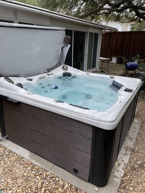 Un bain à remous doté d’un couvercle, installé sur une terrasse avec une plateforme en bois et une bordure en pierre.