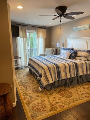 Quarto com cama, ventoinha no teto, mesa de cabeceira, abajur e janela com cortinas.