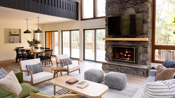 A spacious living room with a stone fireplace, a dining area, and a kitchen with pendant lighting.