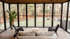 A modern room with large windows, a sofa, two chairs, and a small table.