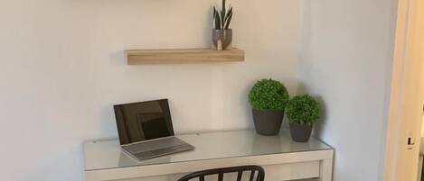 A white desk with a laptop, two potted plants, and a framed picture on a wall.