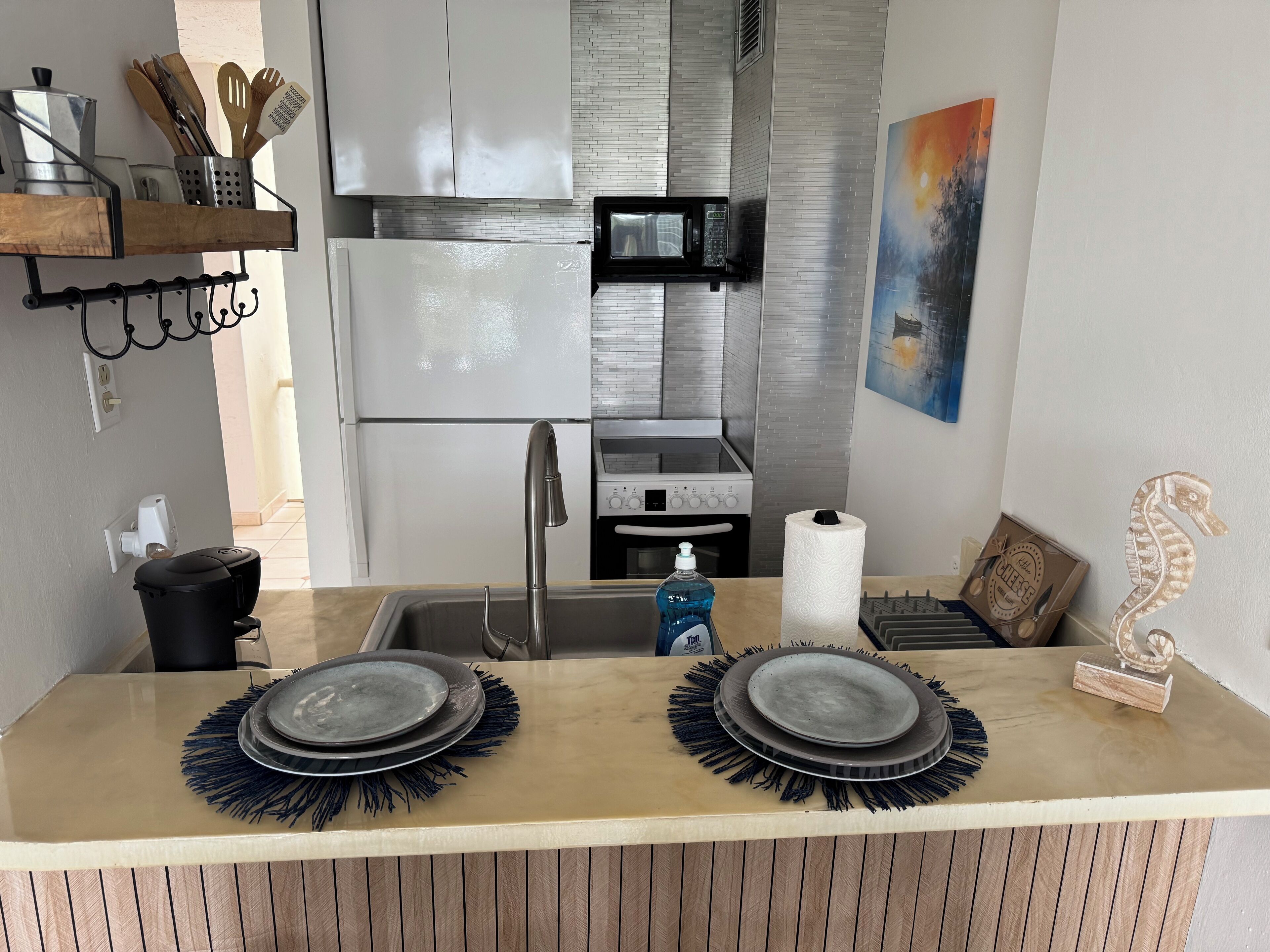 Cozinha moderna com geladeira, micro-ondas e fogão de aço inoxidável. Há duas pratos com borda azul no balcão, um rolo de papel toalha e uma escultura decorativa de cavalo-marinho.