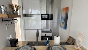 Een moderne keuken met een roestvrijstalen koelkast, magnetron en fornuis. Op het aanrecht staan twee borden met blauwe franjes, een rol keukenpapier en een decoratief zeepaardbeeldje.