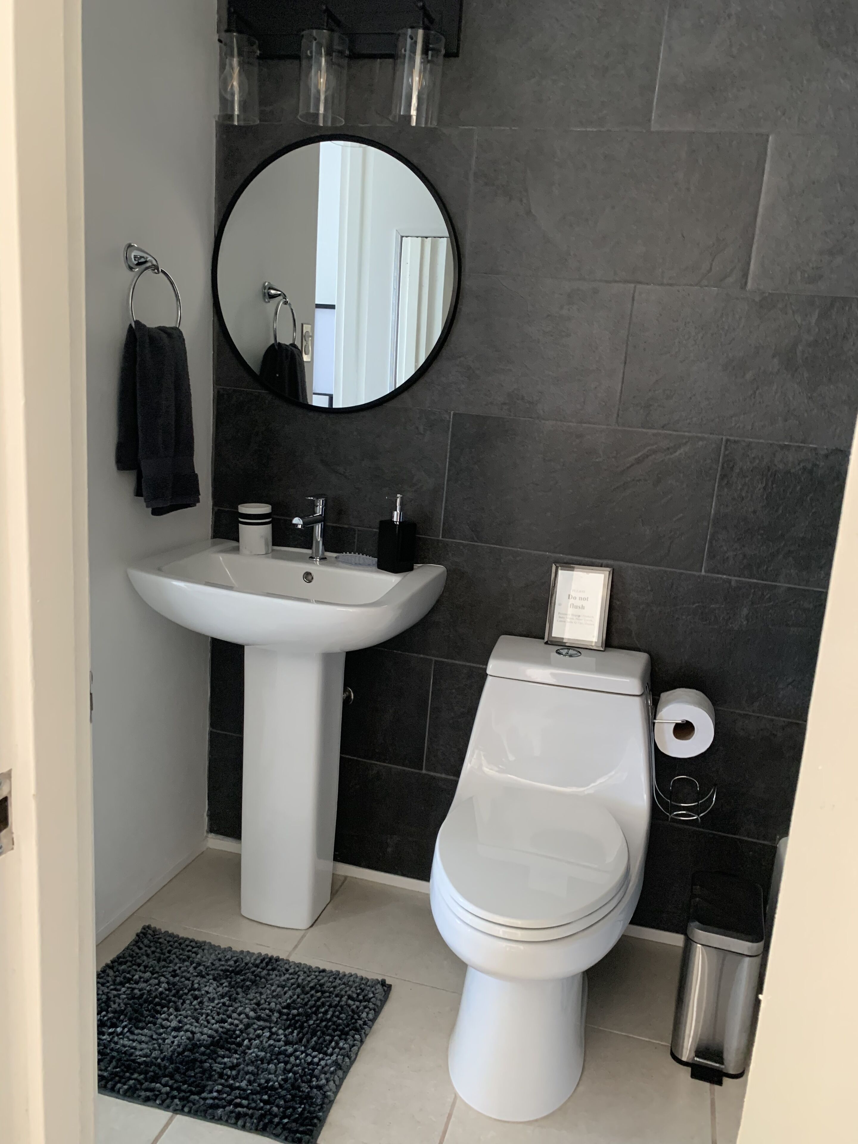 Een badkamer met een wit wastafel, zwarte tegels, een ronde spiegel en een toilet.
