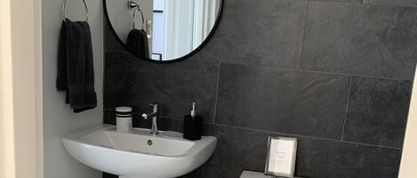 Een badkamer met een wit wastafel, zwarte tegels, een ronde spiegel en een toilet.