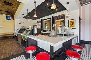 L’intérieur d’un restaurant avec un comptoir, des tabourets rouges, des luminaires suspendus, un menu écrit à la craie et une affiche.