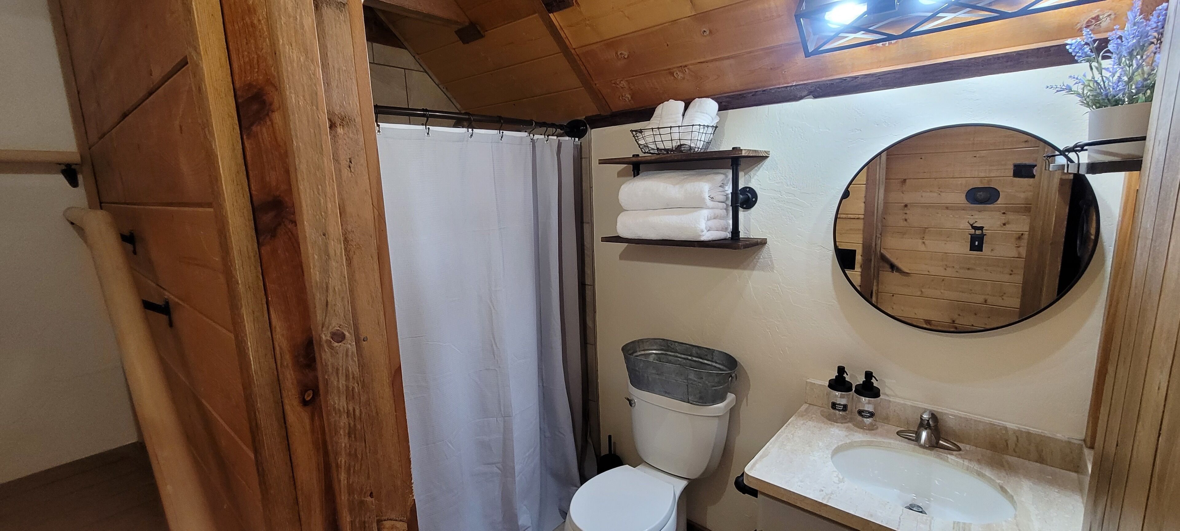 A wooden bathroom with a toilet, a sink, a mirror, and shelves with towels.