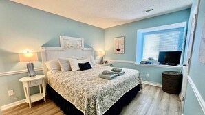 A bedroom with a bed, bedside tables, a window with blinds, and a television.