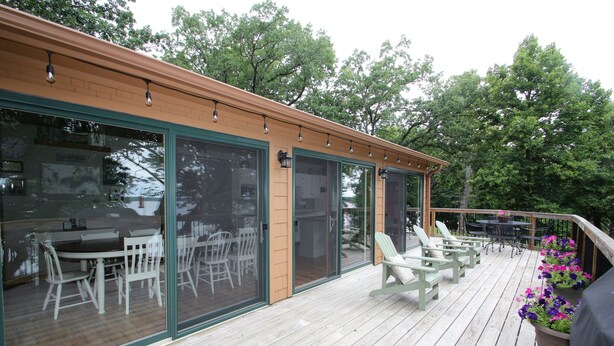 A wooden deck with outdoor furniture, a covered patio area, and a glass door leading to an interior space with a dining table and chairs. - Cabin with amazing views, prime location and privacy! 3 bedrooms 2 bathrooms (Battle Lake)