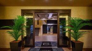 A hotel entrance with a modern design, featuring a glass door, a black doormat with the hotel name, and two potted plants on either side. - HOTEL ZEN Yokohama Hazawa (Yokohama)