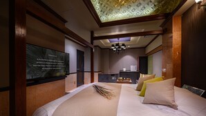 A hotel room with a large bed, a chandelier, a television, and a wall-mounted screen displaying a message. - HOTEL ZEN Yokohama Hazawa (Yokohama)
