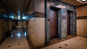 A modern hotel lobby with a marble floor, two elevators, and a long corridor with potted plants. - HOTEL ZEN Yokohama Hazawa (Yokohama)