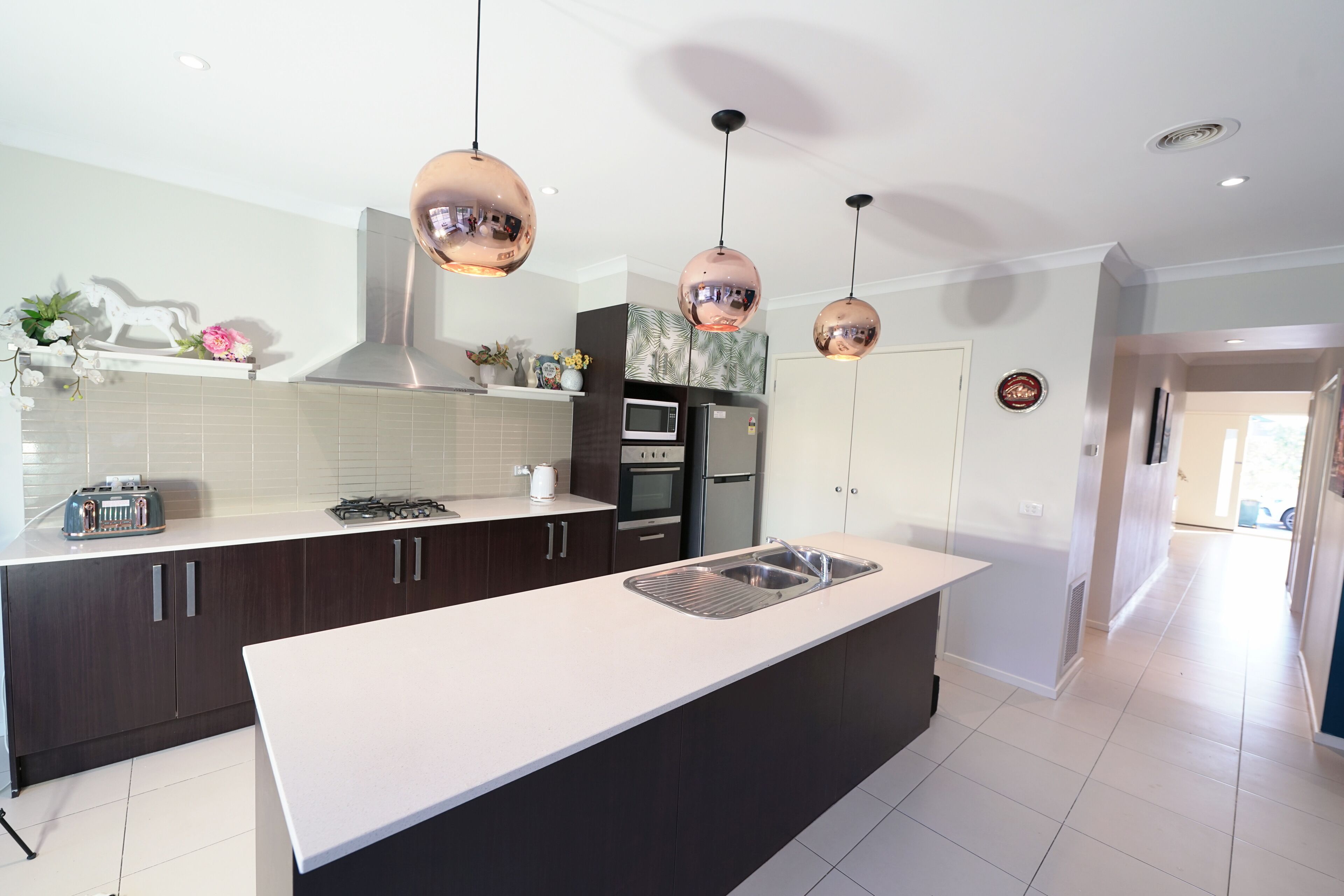 A modern kitchen with dark cabinets, a white countertop, stainless steel appliances, and copper pendant lights.