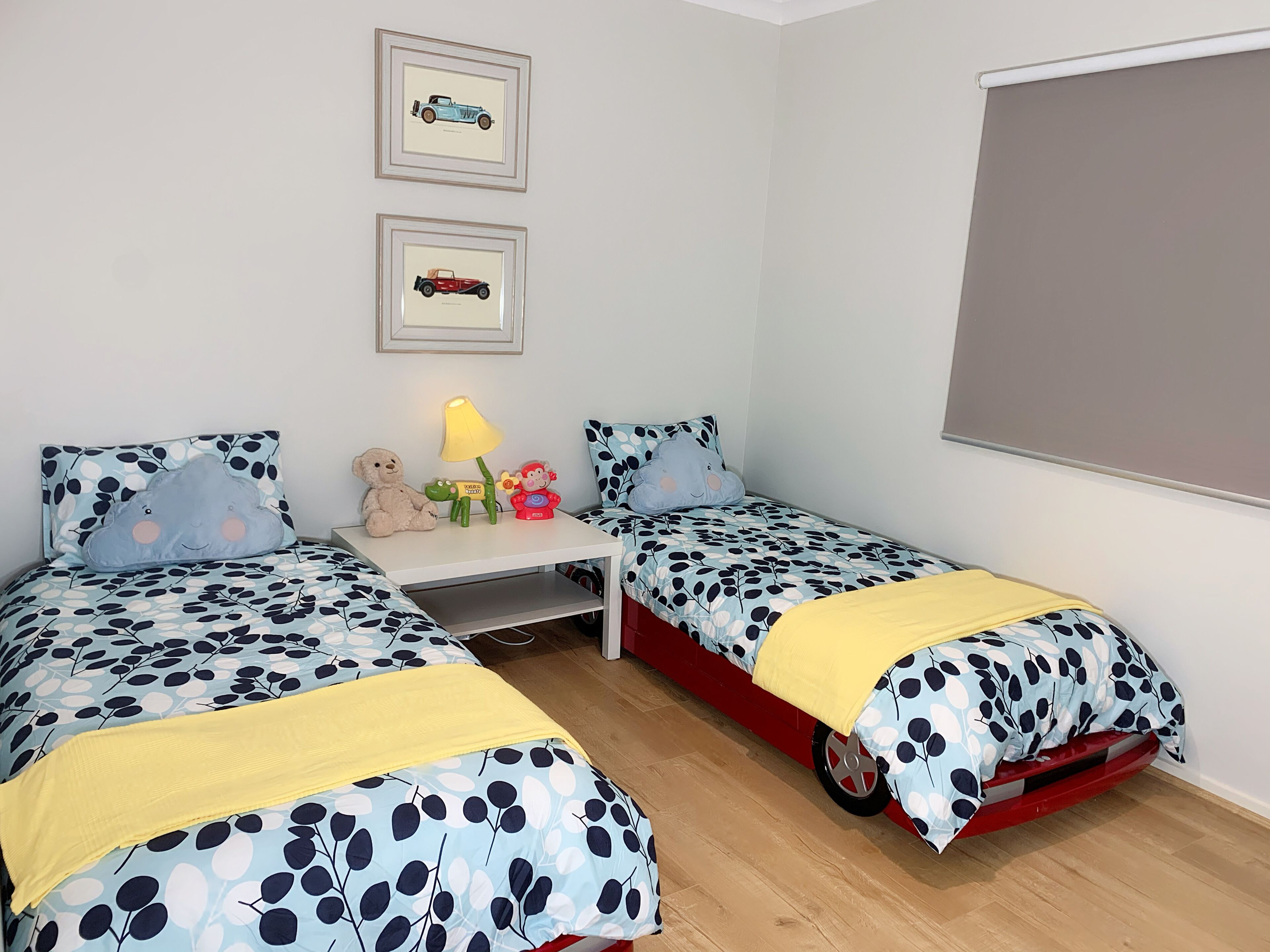 A bedroom with two beds, a nightstand, a lamp, and wall art.