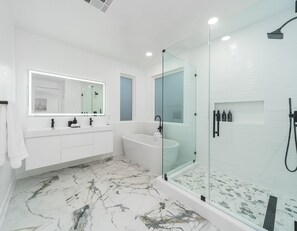A modern bathroom with a glass-enclosed shower, a freestanding bathtub, and a vanity with a large mirror.