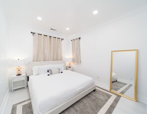 A modern bedroom with a large bed, two bedside tables with lamps, a large mirror, and a geometric-patterned rug.