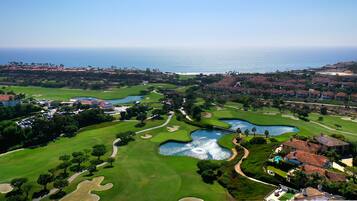 A golf course with multiple bunkers and water hazards, surrounded by residential areas and a view of the ocean.