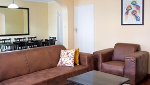 Una sala de estar con un sofá de cuero marrón, un sillón a juego, una mesita y un comedor con sillas y una mesa.