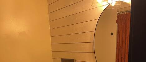 Et badeværelse med trævæg, toilet, vask med spejl og en kurv med håndklæder.