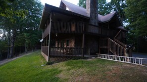 Una cabaña de madera de dos pisos con chimenea de piedra, un balcón y una escalera que conduce al nivel superior.