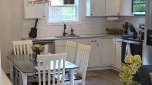 A modern kitchen with white cabinetry, a dining area with a wooden table and chairs, and a grey sofa in the living area. - Porchland Cottage -PRACTICALLY NEW HOUSE with Countryside view -pet friendly (Portland)