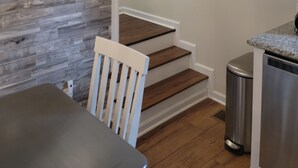 A staircase with wooden steps and white railings, leading to a kitchen area with a stainless steel refrigerator and a trash can. - Porchland Cottage -PRACTICALLY NEW HOUSE with Countryside view -pet friendly (Portland)