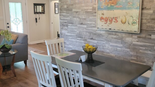 A dining area with a dark wooden table, white chairs, and a decorative wall with a vintage-style painting. - Porchland Cottage -PRACTICALLY NEW HOUSE with Countryside view -pet friendly (Portland)