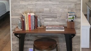 A room with a wooden wall, a round table with books, a stool, and a wall-mounted painting. - Porchland Cottage -PRACTICALLY NEW HOUSE with Countryside view -pet friendly (Portland)