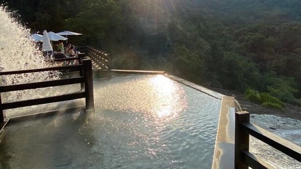 A wooden deck overlooking a river with a view of the sun setting behind a mountain range.